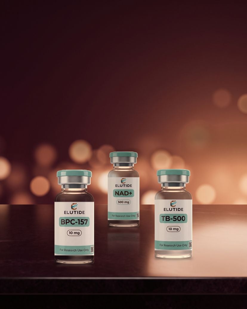 Three sealed Elutide research vials, BPC-157, NAD+ and TB-500, on a dark bench in warm copper light.